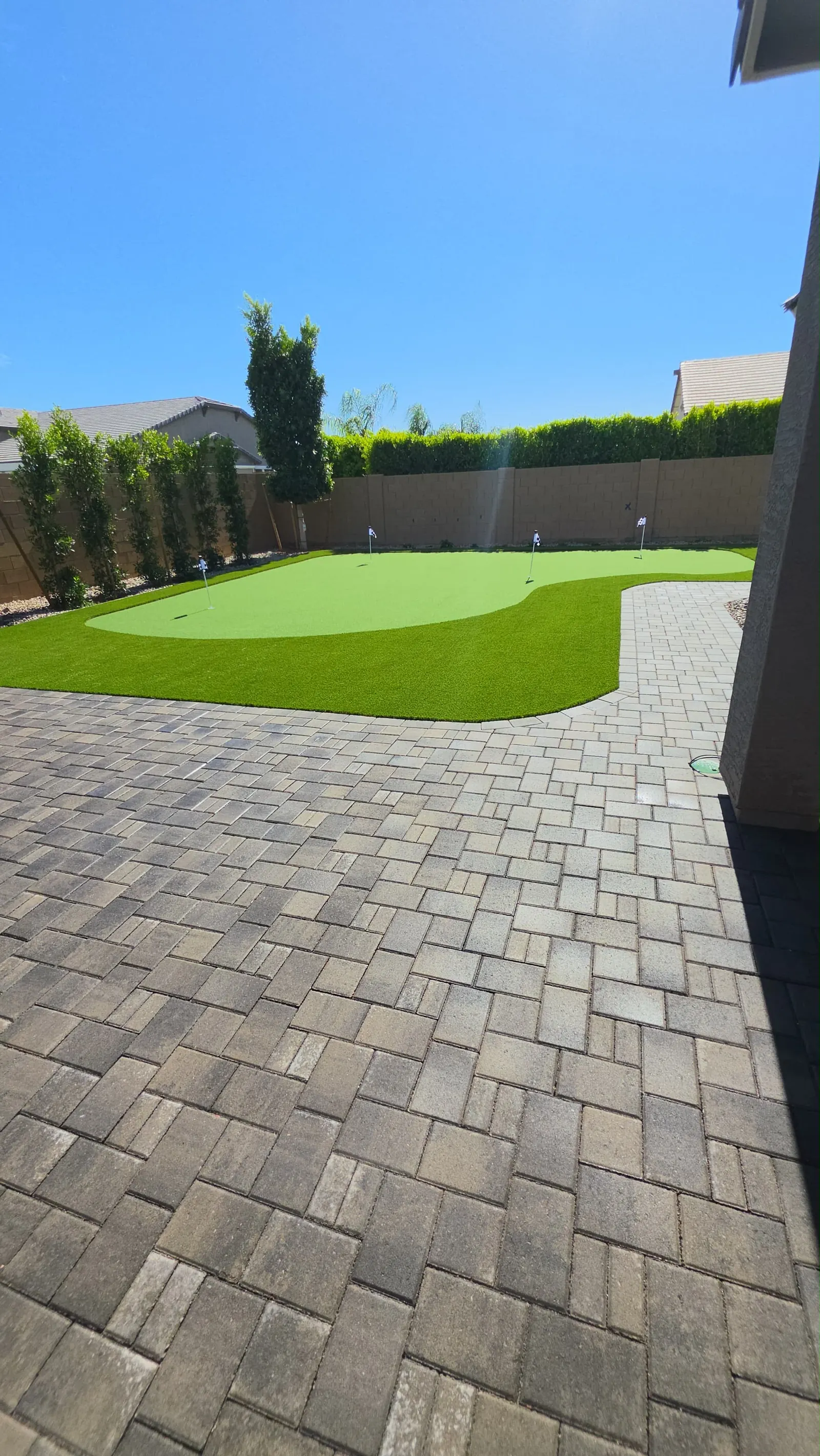 Gray paver patio curving around a backyard putting green